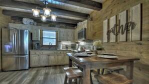 Une cuisine rustique avec des meubles en bois, un réfrigérateur en acier inoxydable, une table en bois avec des tabourets et un panneau décoratif sur le mur portant l'inscription « Gather ».