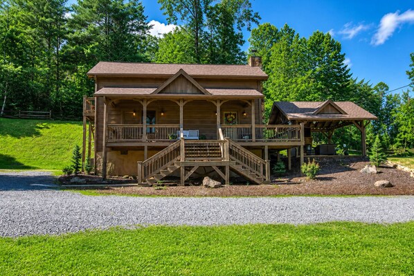 A two-story log cabin with a porch, a covered deck, and a gravel driveway. - Farmhouse Cabin, Hot Tub, Fireplace Patio w/TV (Blue Ridge)