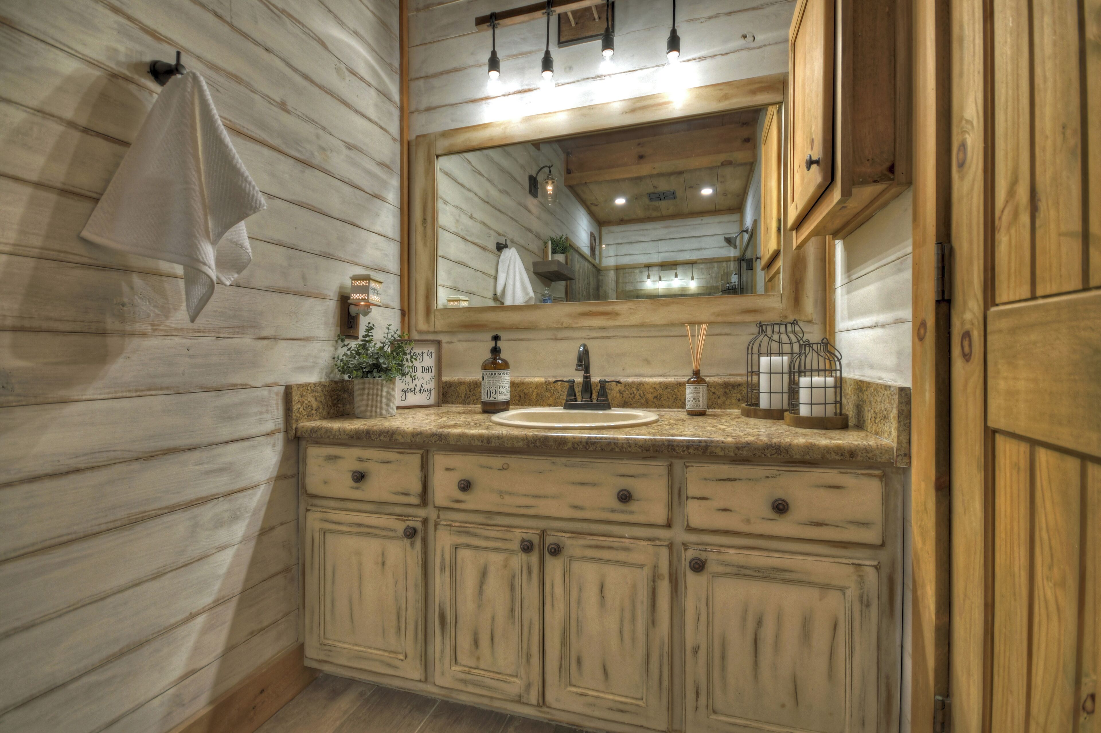 A rustic bathroom with wooden walls, a large mirror, a sink with a bottle of hand soap, and a towel hanging on the wall.