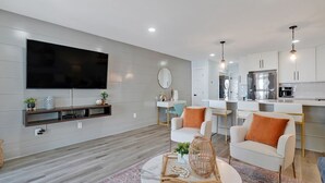 Un soggiorno moderno con una TV a schermo piatto, un tavolino da caffè con oggetti decorativi e un'area pranzo con arredi bianchi.