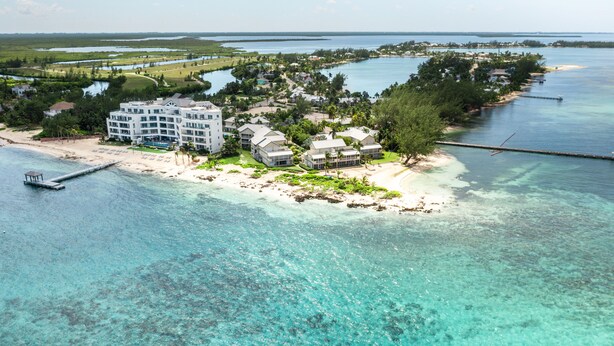 An aerial view of a coastal resort with multiple buildings, a pier, and clear turquoise waters. - Oceanfront right next to RumPoint, tranquility,pool,gym,tennis court and sunsets (Rum Point)