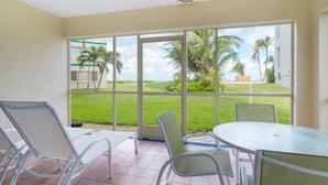 A room with a glass door leading to a balcony with a view of a lawn and palm trees. - Oceanfront right next to RumPoint, tranquility,pool,gym,tennis court and sunsets (Rum Point)