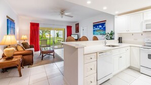 A modern kitchen with white cabinets, a built-in dishwasher, and a large island. There is a dining area with a red curtain and a sofa. - Oceanfront right next to RumPoint, tranquility,pool,gym,tennis court and sunsets (Rum Point)