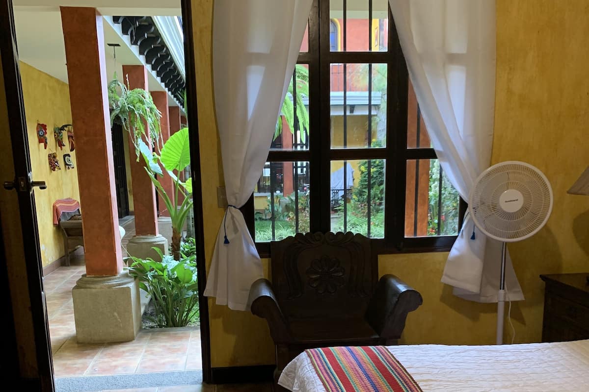 Ein Hotelzimmer mit Bett, Stuhl, Ventilator und Blick ins Freie.