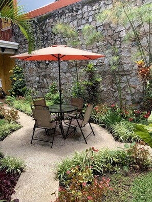 A patio with a table and chairs under an umbrella, surrounded by various plants and a stone wall. - Casa El Conquistador (Antigua Guatemala)