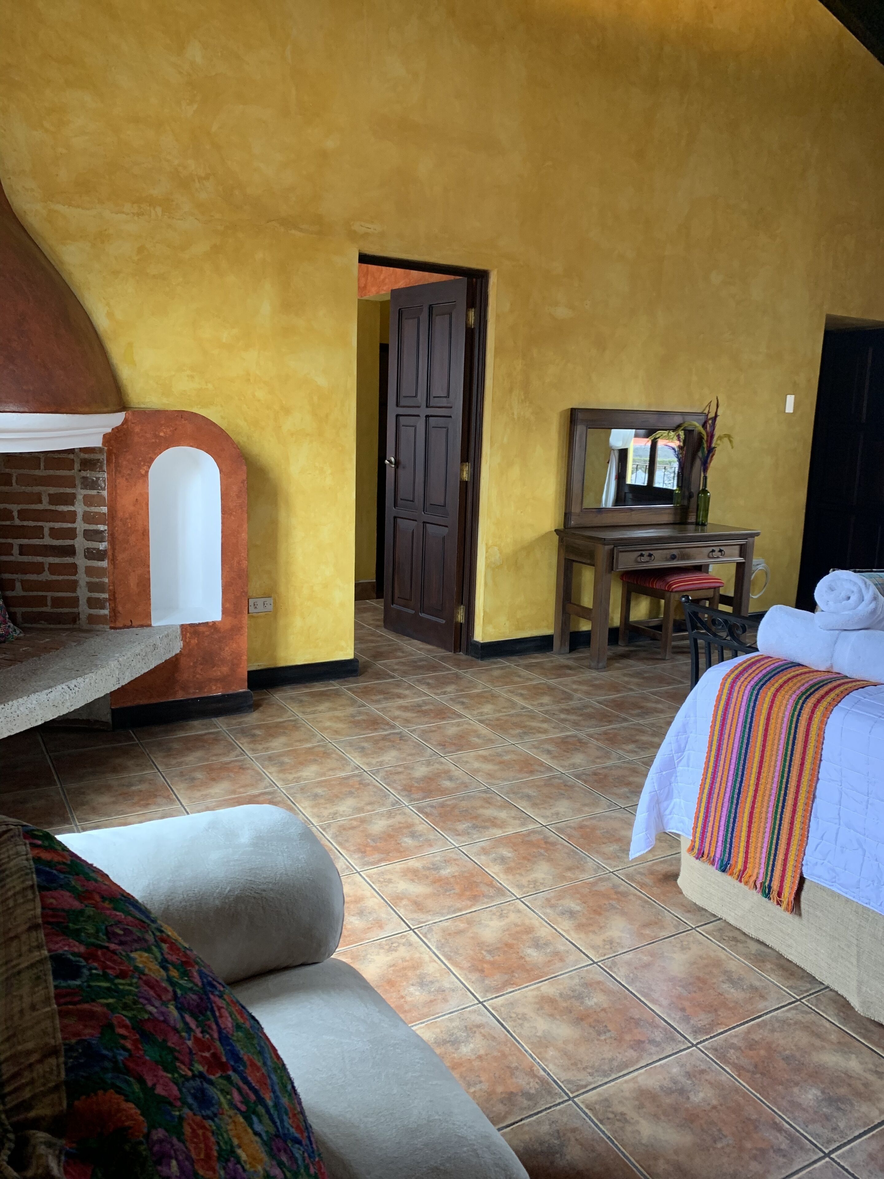 A room with a bed, a chair, a small table, and a door leading to another room.