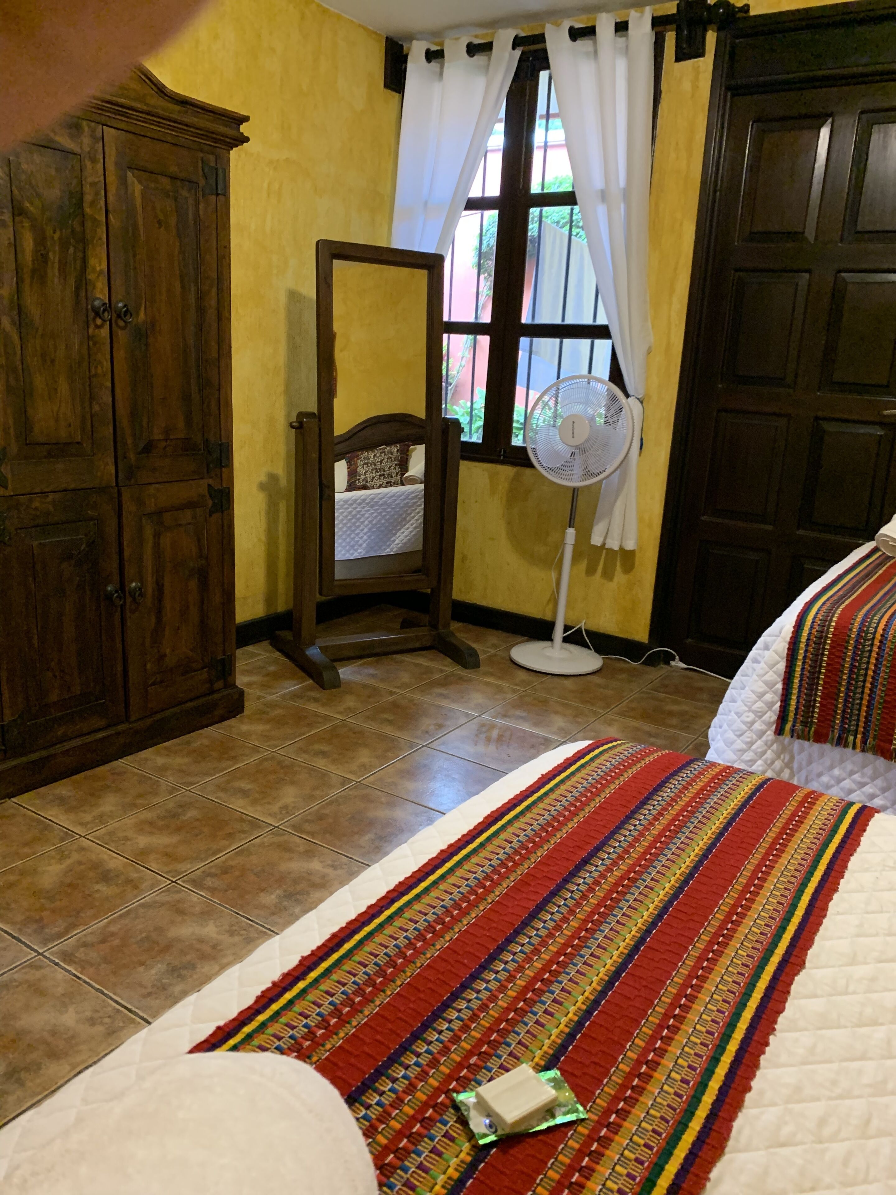 Une chambre à coucher comprenant un lit, une table de chevet, un miroir, un ventilateur sur pied et une armoire.