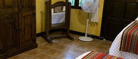 Une chambre à coucher comprenant un lit, une table de chevet, un miroir, un ventilateur sur pied et une armoire.