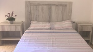 Un lit avec une couvre-lit à rayures, deux tables de chevet et une plante en pot sur la table de chevet de gauche.
