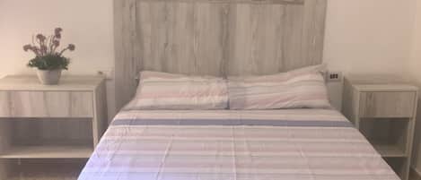 A bed with a striped bedspread, two nightstands, and a potted plant on the left nightstand.