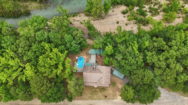 Vista aérea de una zona residencial con piscina, un porche cubierto y abundante vegetación circundante.
