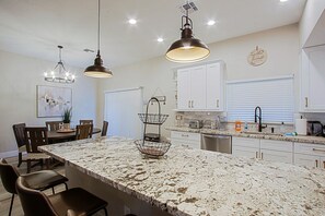 Una cocina con una isla grande, armarios blancos e iluminación colgante.