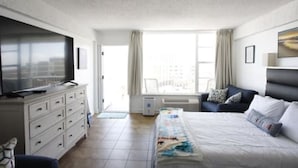 Een hotelkamer met een bed, een televisie op een dressoir, een raam met gordijnen en een stoel.