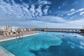 A clear blue pool with lounge chairs and a view of the ocean.