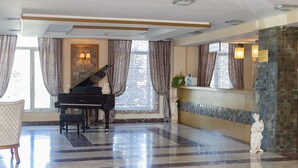 Un vestíbulo imponente con un piano de cola, suelo de mármol y una estatua.