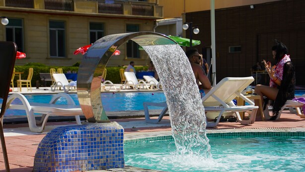 Una piscina con fuente, sillas de descanso y zona empavedada.
