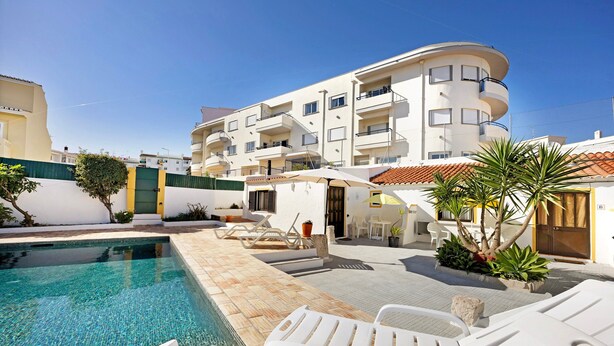 A pool area with lounge chairs, a small table, and a building with balconies. - Apartment 'A Cerca - A' close to the Beach with Shared Pool & Wi-Fi (Lagos)