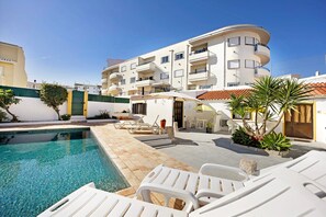 A pool area with lounge chairs, a small table, and a building with balconies. - Apartment 'A Cerca - A' close to the Beach with Shared Pool & Wi-Fi (Lagos)