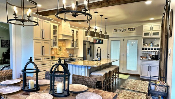 Una cocina amplia con una isla central, una mesa de comedor de madera y taburetes de bar. Hay luces colgantes y un cartel que dice "SOUTHERN FOOD".