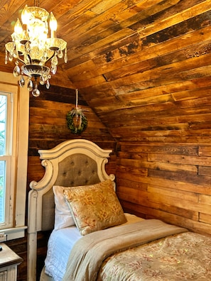 A wooden cabin bedroom with a bed, a chandelier, and a window.