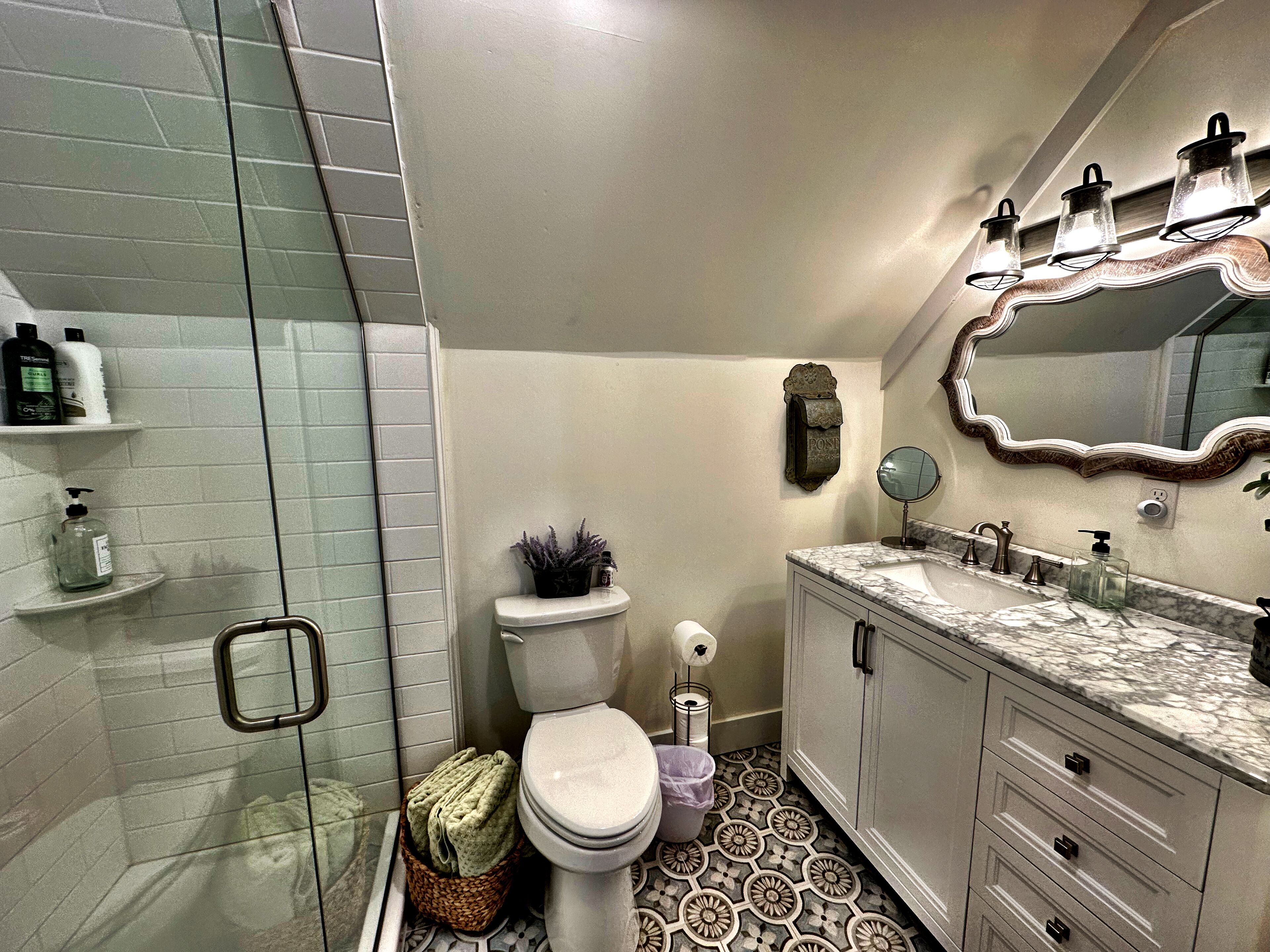 A bathroom with a shower, toilet, vanity, and a mirror.
