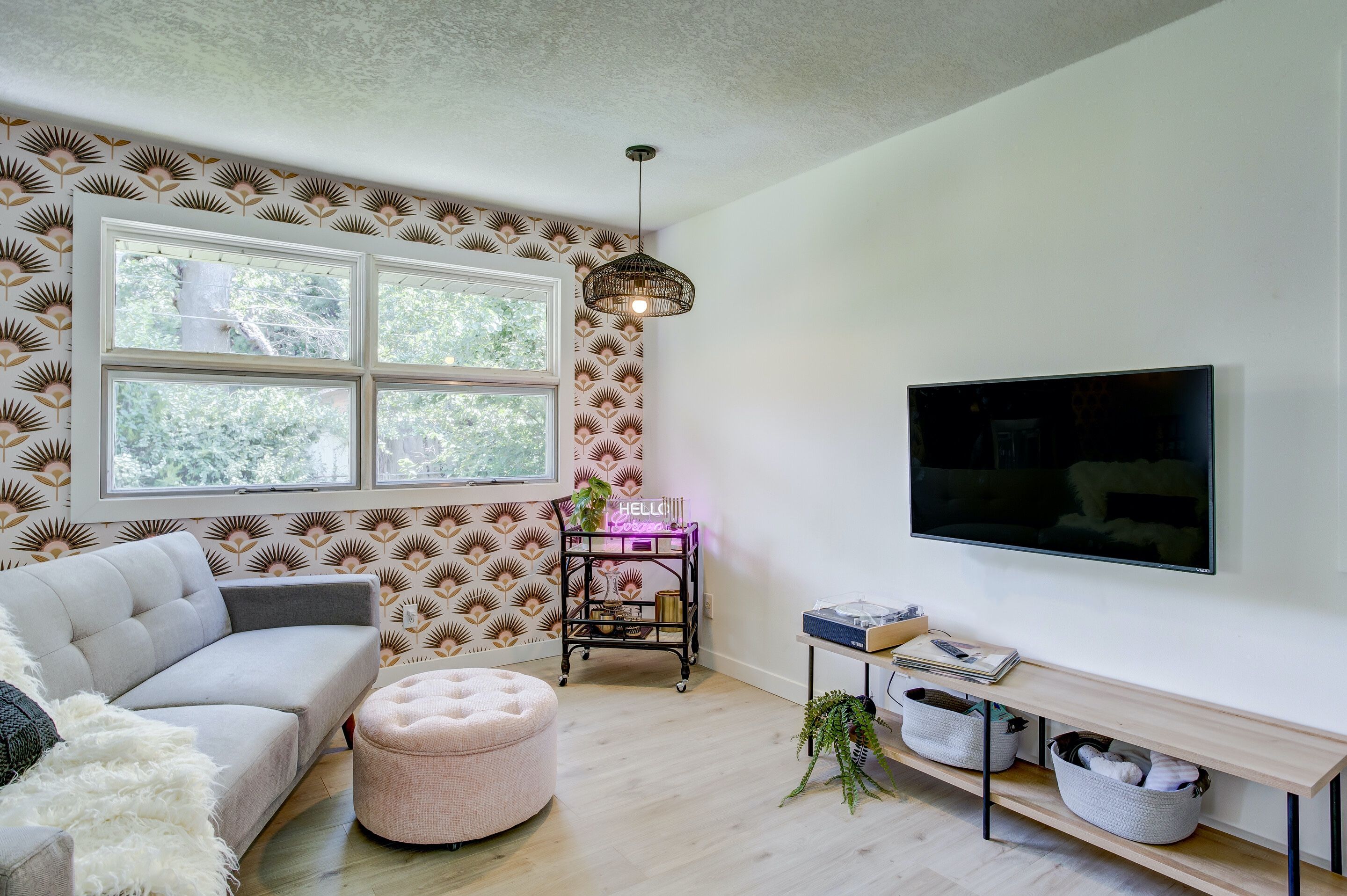 A modern living room with a sofa, ottoman, and a TV mounted on the wall.