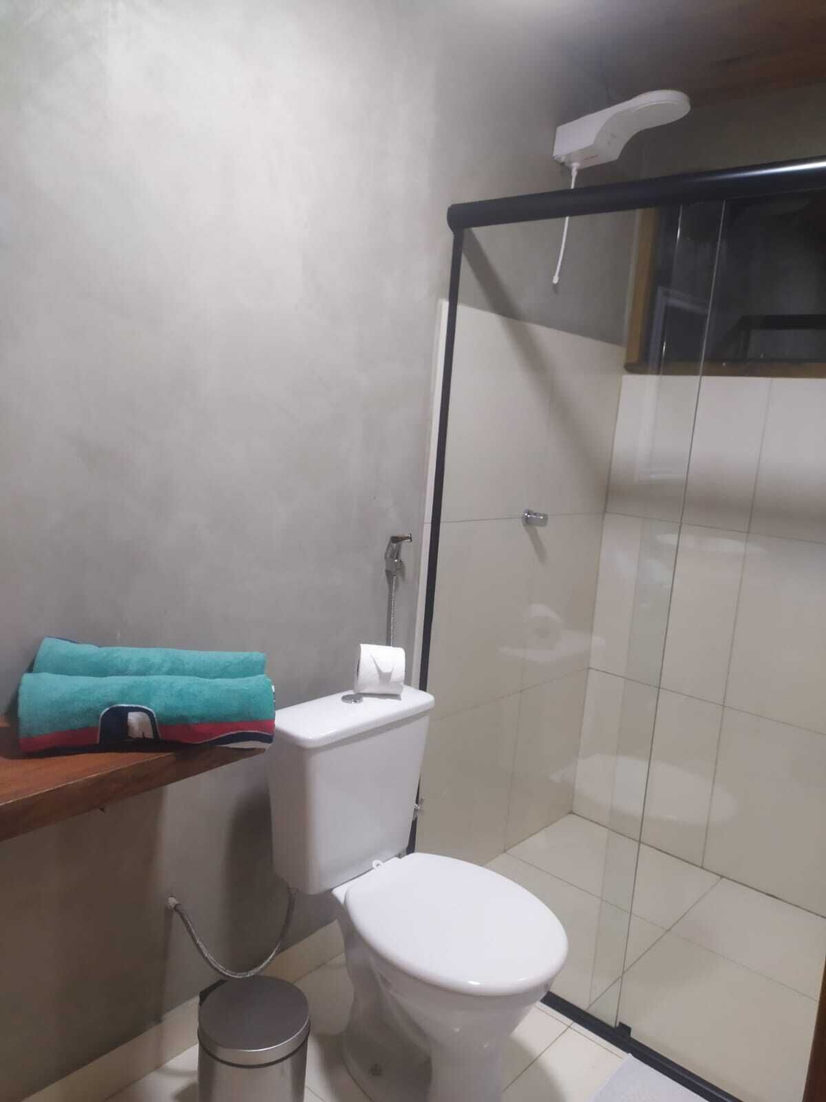 A small bathroom with a toilet, a shower, and a towel on a shelf.