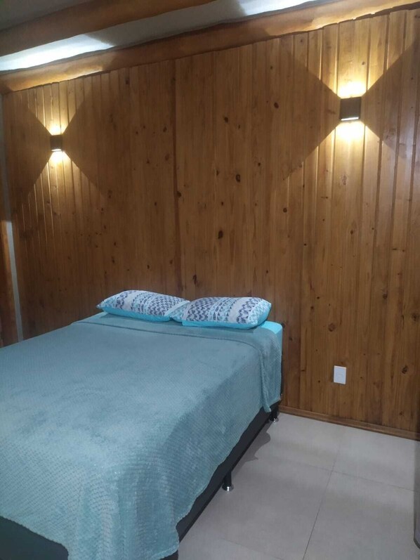 A bedroom with a bed, wooden walls, and two wall-mounted lights.