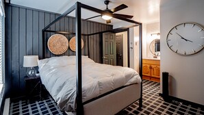 A four-poster bed with a ceiling fan, a round wall clock, and a checkered floor pattern.
