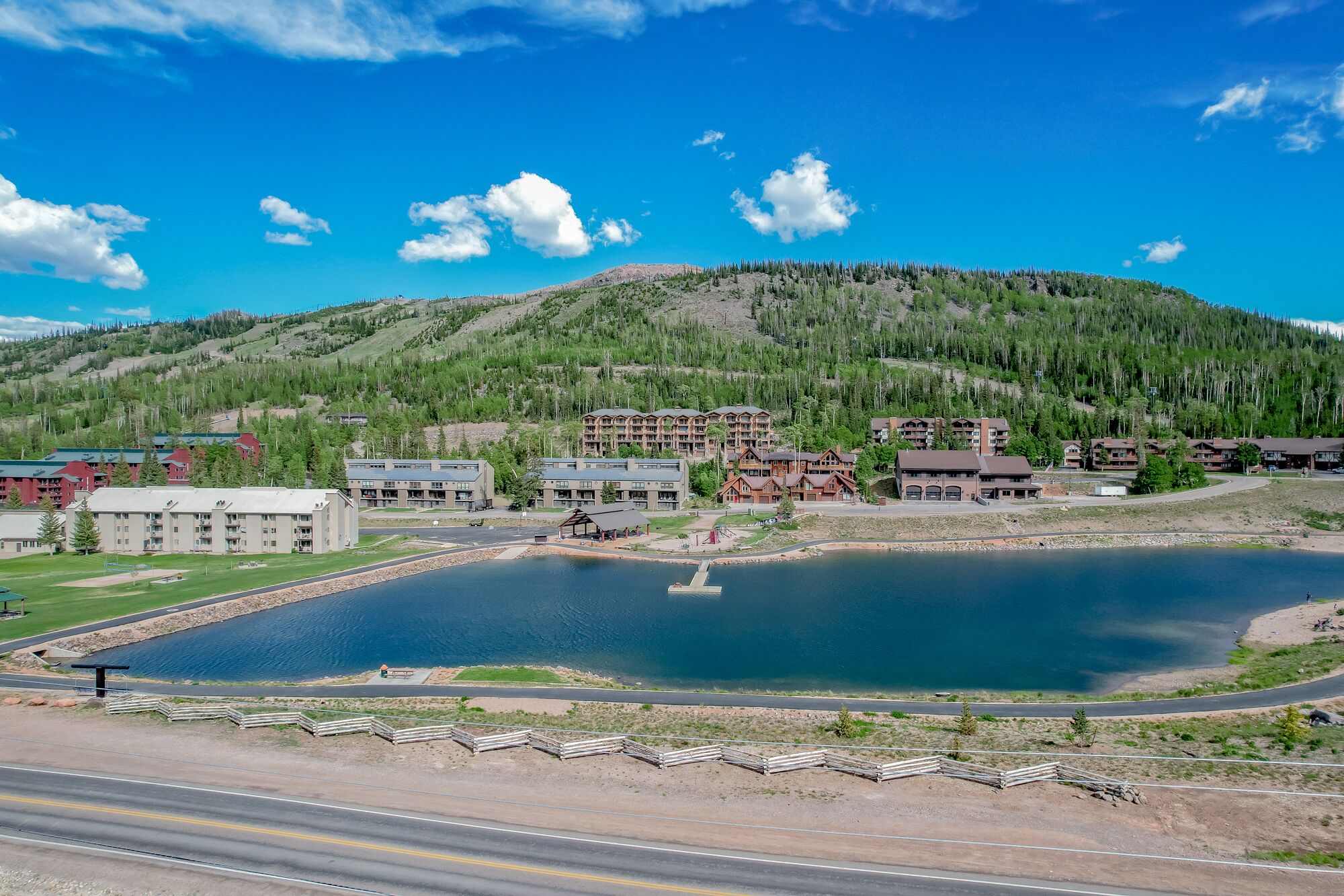 A lakeside resort with multiple buildings, including a lodge and a hotel, surrounded by a forested hillside.