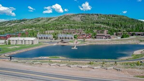 A lakeside resort with multiple buildings, including a lodge and a hotel, surrounded by a forested hillside.