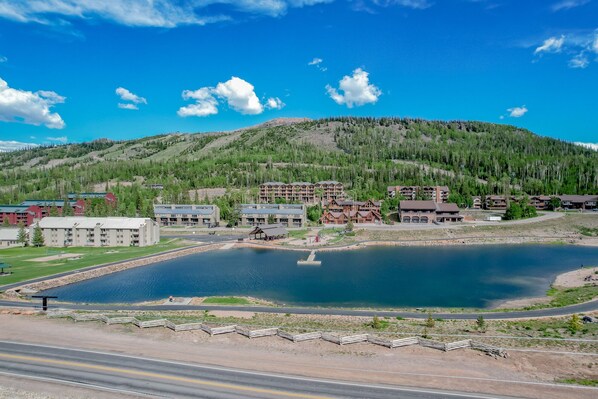 A lakeside resort with multiple buildings, including a lodge and a hotel, surrounded by a forested hillside.