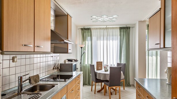 A kitchen with wooden cabinets, a sink, a dining table with chairs, and a window with curtains.