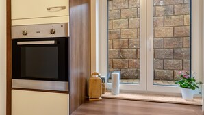 A kitchen with an oven, a wooden cabinet, a window with a stone wall view, and a potted plant on the windowsill. - Holiday Apartment "Im Bubenstück" with Wi-Fi (Bingen)