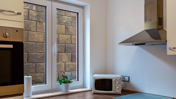 A kitchen with a microwave, oven, and a window with a brick wall view. - Holiday Apartment "Im Bubenstück" with Wi-Fi (Bingen)