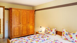 Una camera da letto con un'armadiatura in legno, un letto con biancheria da letto a motivi floreali, una lampada da comodino e un tavolino da notte.