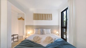 Habitación de hotel con cama, mesitas de noche, toallero y ventana con cortinas.