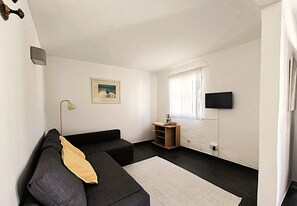 A living room with a sofa, a small table, a TV mounted on the wall, and a window with curtains. - Studio Apartment 'A Cerca - F' with Pool, Garden & Wi-Fi (Lagos)