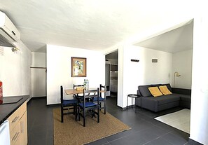 A modern living room with a sofa, a dining table with chairs, a kitchen area, and a staircase leading to an upper level. - Studio Apartment 'A Cerca - F' with Pool, Garden & Wi-Fi (Lagos)
