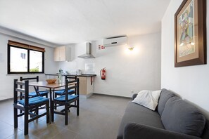 A modern kitchen with a dining area, a gray sofa, and a fire extinguisher on the wall. - Studio Apartment 'A Cerca - F' with Pool, Garden & Wi-Fi (Lagos)
