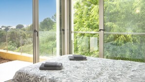 Un dormitorio con un ventanal grande, una cama con colcha estampada y dos toallas dobladas.
