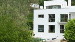 Un edificio moderno de color blanco con varias ventanas, una piscina y un jardín con sillas de descanso.
