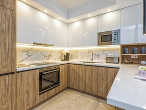 Una cocina moderna con armarios blancos, microondas, lavamanos y detalles de madera.