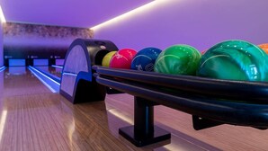 Une salle de bowling avec un plancher en bois et une rangée de boules de bowling colorées, rangées sur un présentoir.