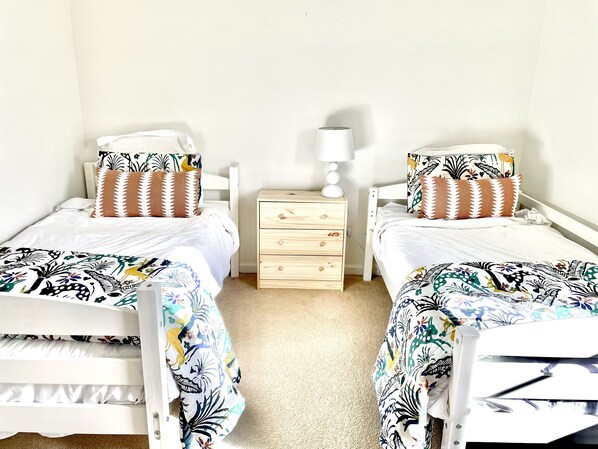 A twin bedroom with two beds, each with a patterned bedspread and matching pillows, a wooden nightstand with a lamp, and a plain wall. - Spacious home at the base of the Blue Ridge Mountains near LU (Lynchburg)