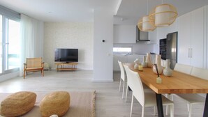 A modern living room with a TV, seating, and a dining area with a table and chairs. - 2202 Modern Apartment with Panoramic Sea Views (Cancelada Estepona)