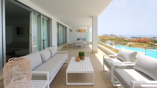 A modern balcony with a sofa, chairs, a table, and a view of the ocean and buildings. - 2202 Modern Apartment with Panoramic Sea Views (Cancelada Estepona)
