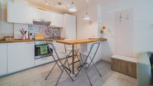 Une cuisine moderne avec des meubles blancs, un plan de travail en bois, un four encastré et une table à manger pliante avec des chaises.