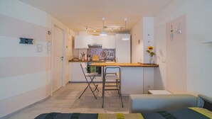 Une pièce compacte comprenant un coin cuisine, un espace repas avec une table et des chaises, et un lit avec une couverture à rayures.