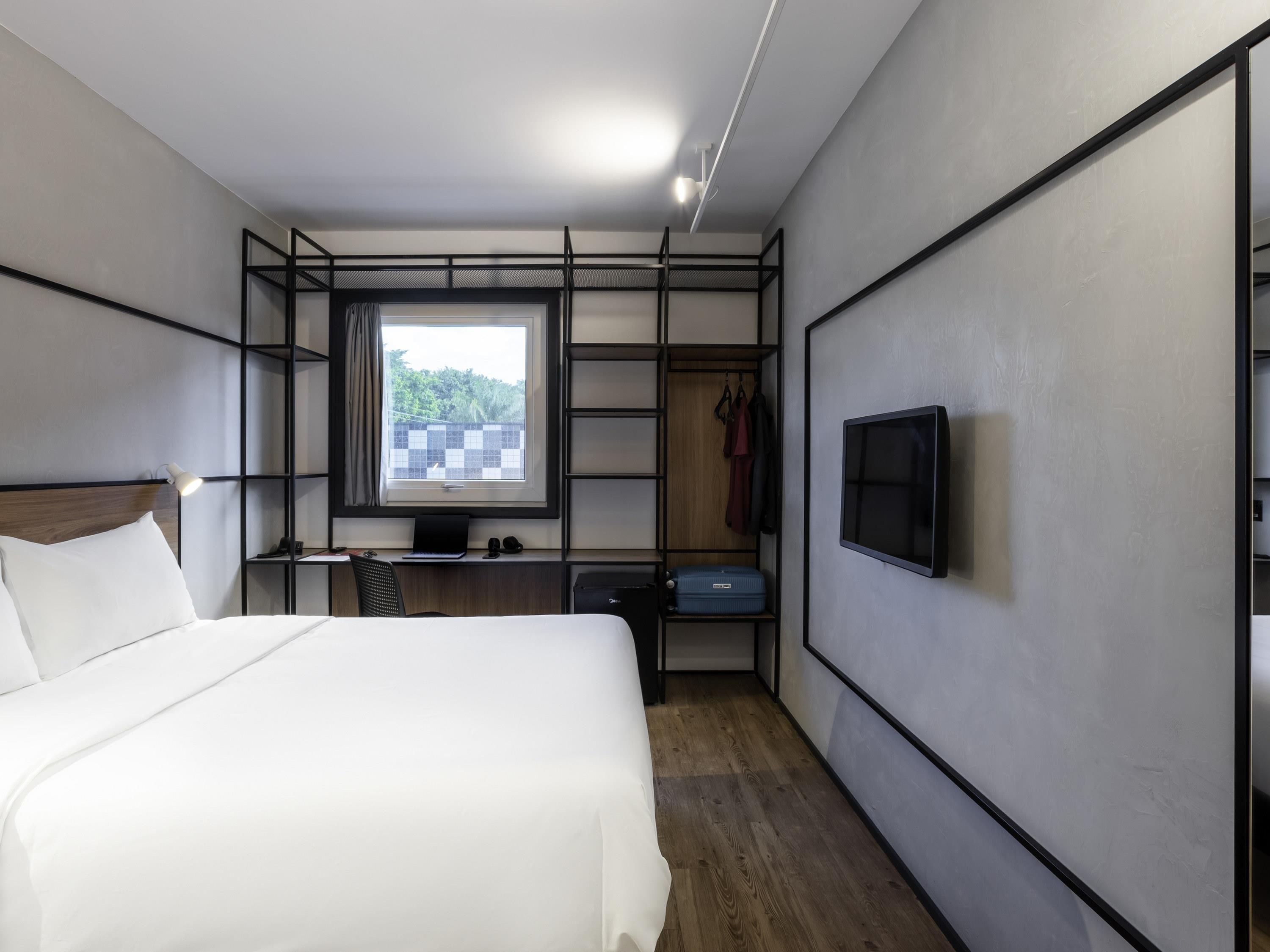 Een moderne hotelkamer met een bed, een bureau met een computer, een televisie en een kledingkast.